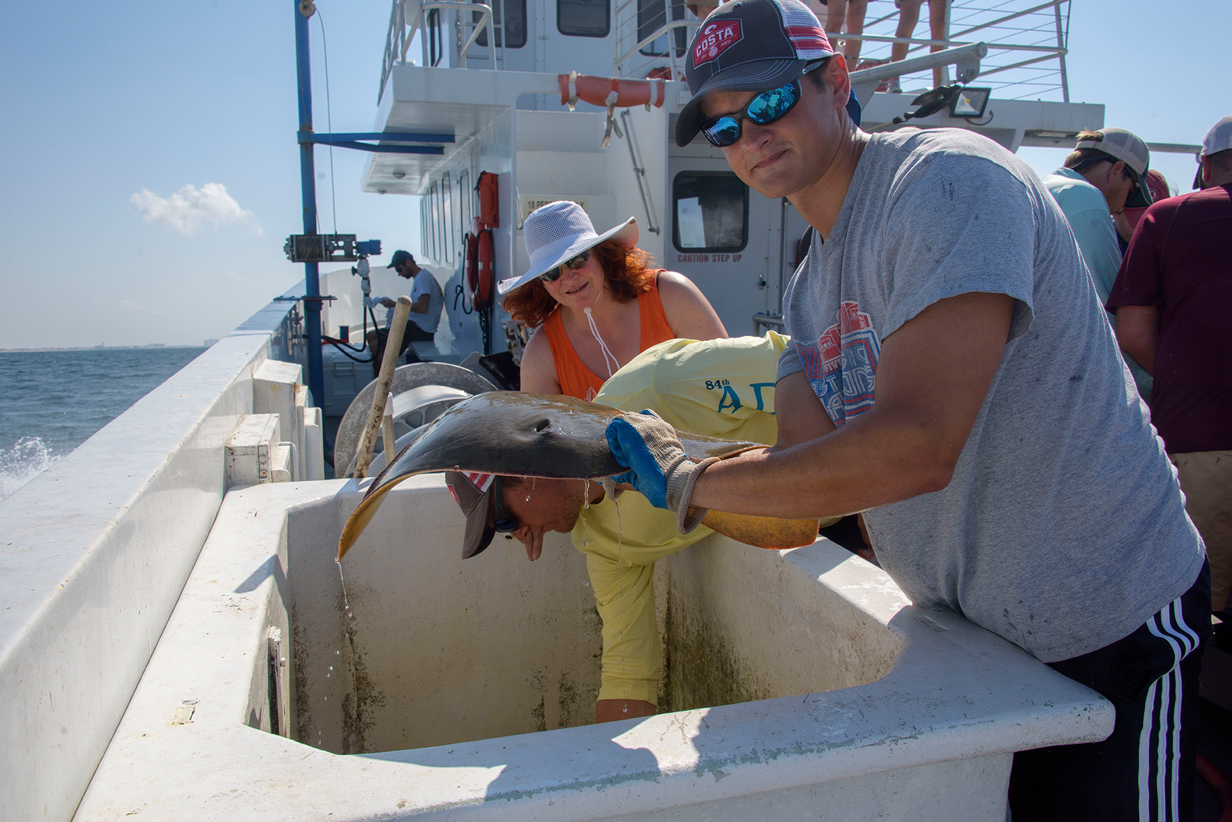 A man holds a stingray aboard a boat.