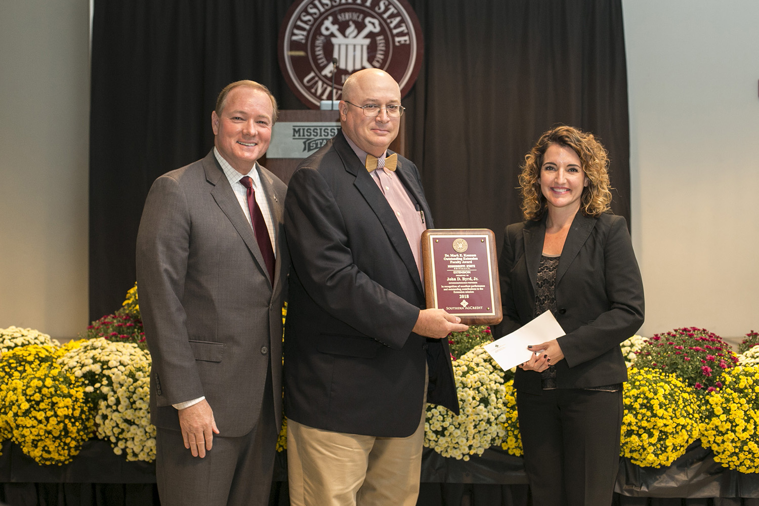 Three adults pose during a plaque presentation. 