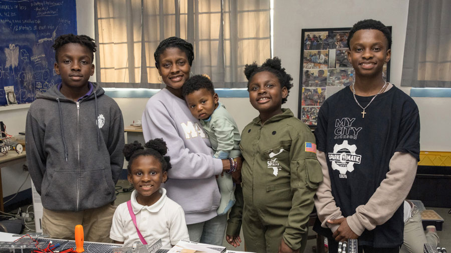 A family, including three sons, two daughters, and one mom, standing smiling in a classroom.