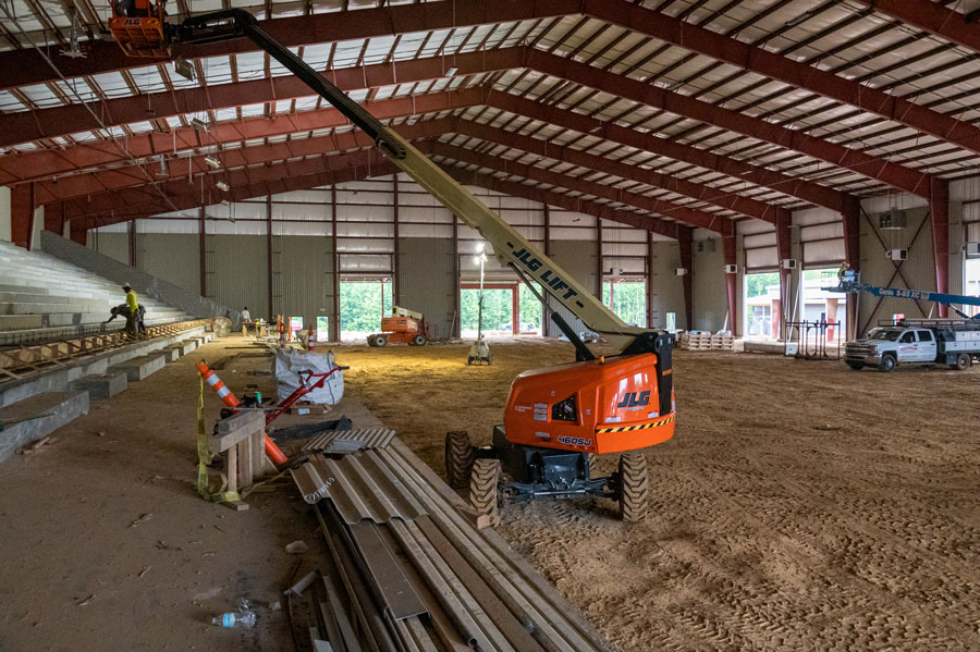 Three manlifts at a construction site with a few workers in hardhats.