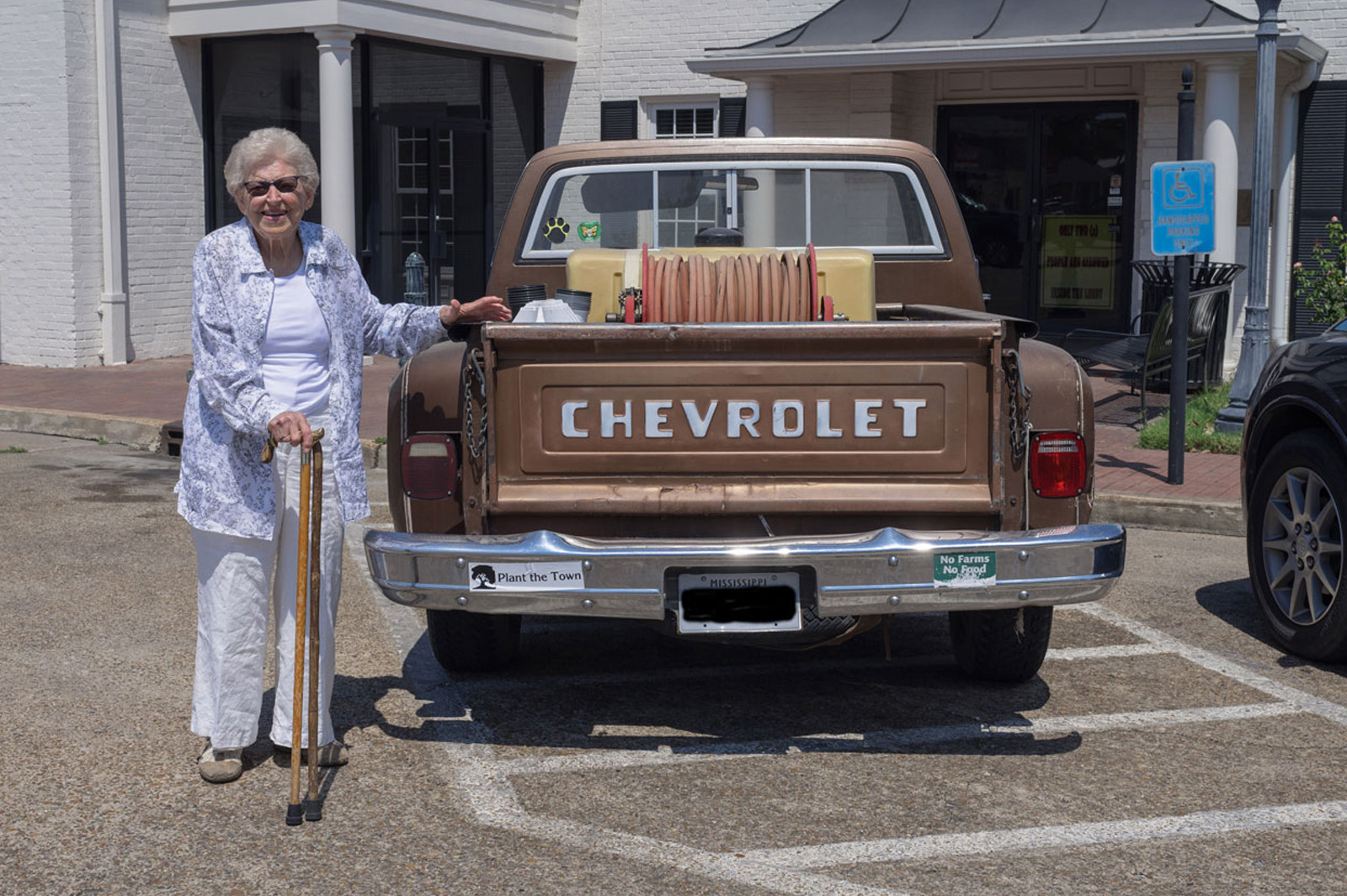 A woman with a cane standing beside an old pickup truck.