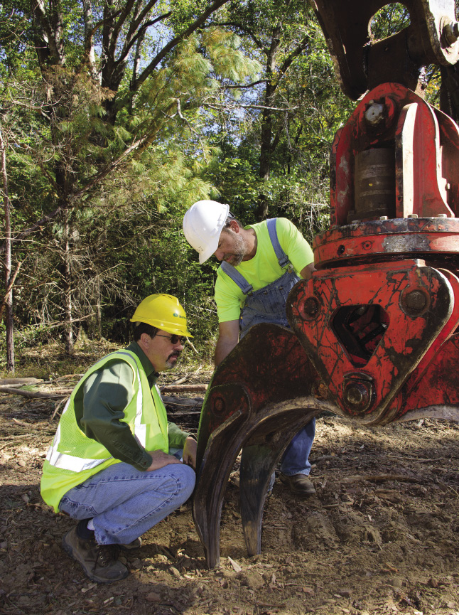 two men in hard hats and bright green clothing inspect logging equipment.