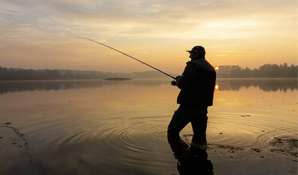Man fishing in water at sunset.