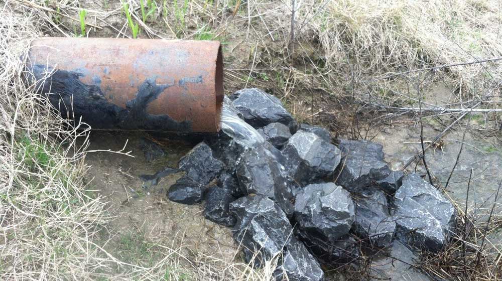 Water flows out of a pipe onto large rocks.