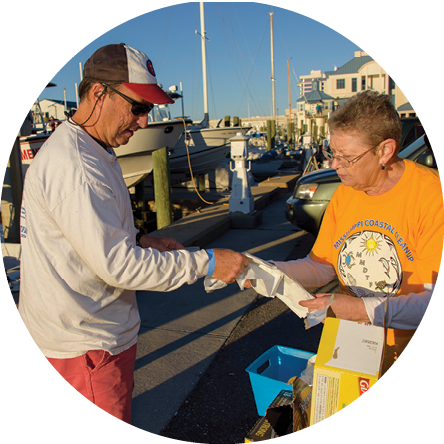 A person gives a trash bag to another person at a boat dock.