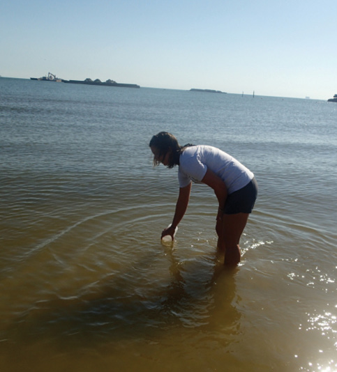 A researcher stands shin-deep in water to fill a jar.