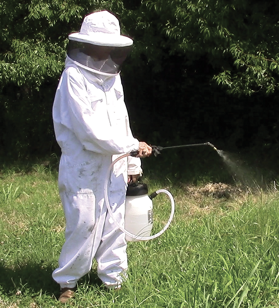 A man in a protective suit sprays liquid from a tank.