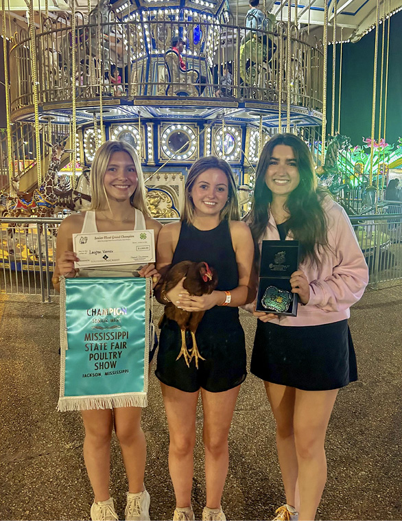 An older participant poses with two friends. They are showing the prize, chicken, and belt buckle.