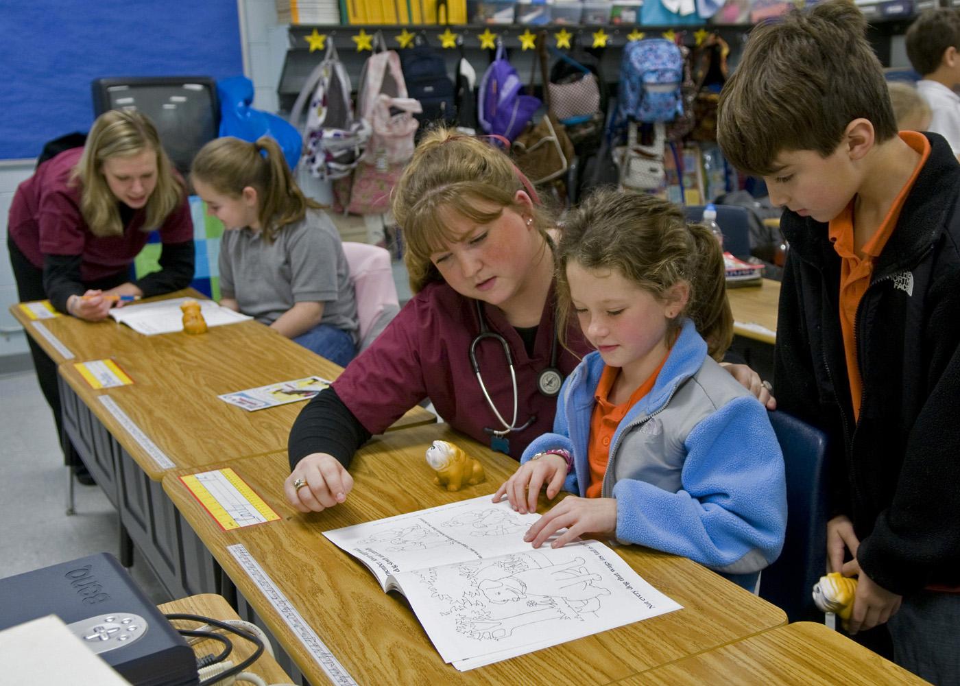 MSU veterinary student Shannon Vawter of Horn Lake works with third grade Starkville Academy students Carly Smith and Montana Brasher while MSU student Katie Ebers of Jackson (background) spends a moment with elementary student Mallory Barber. (Photo by Tom Thompson)