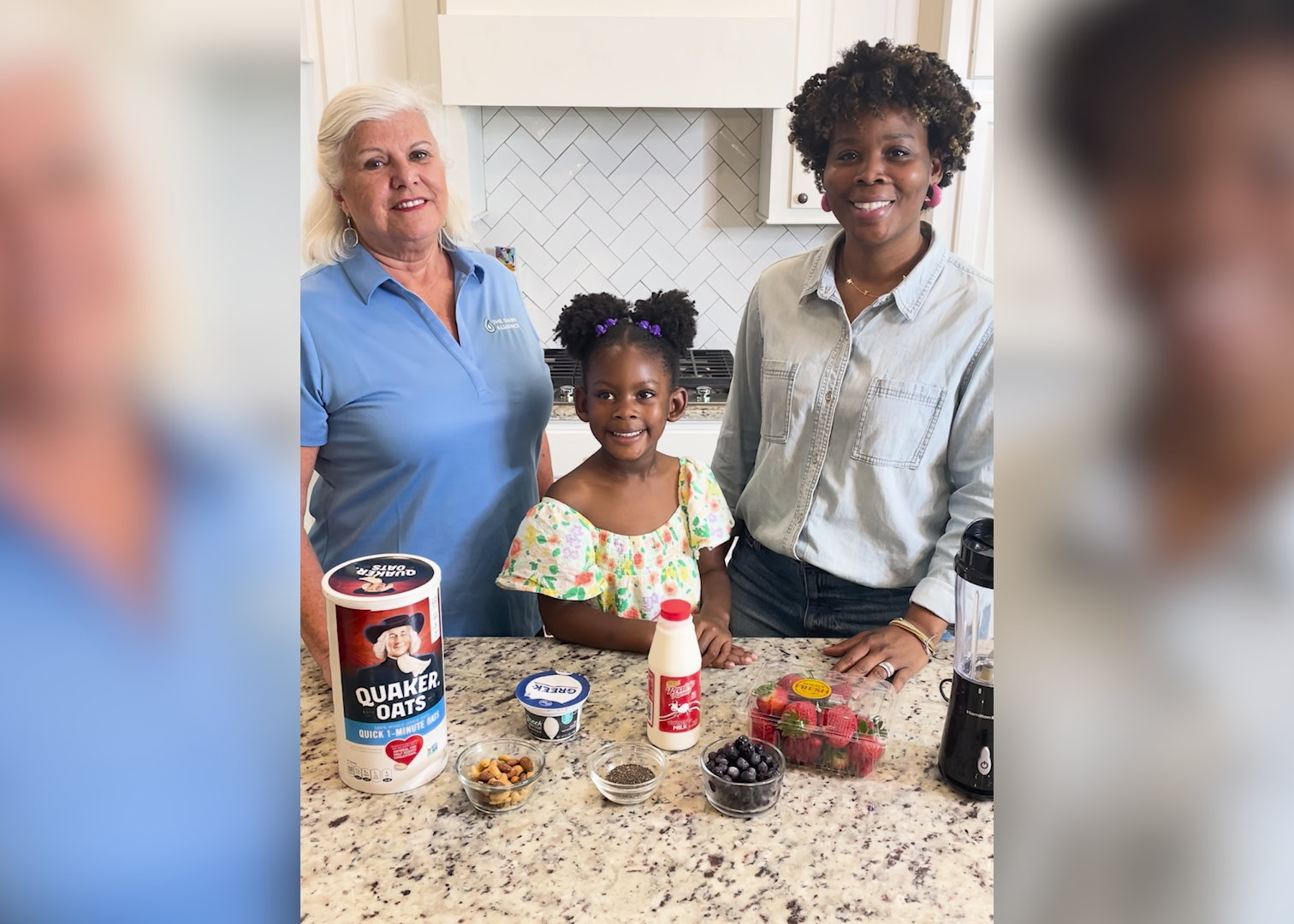 Two women and a child stand behind a kitchen counter filled with ingredients to make a smoothie