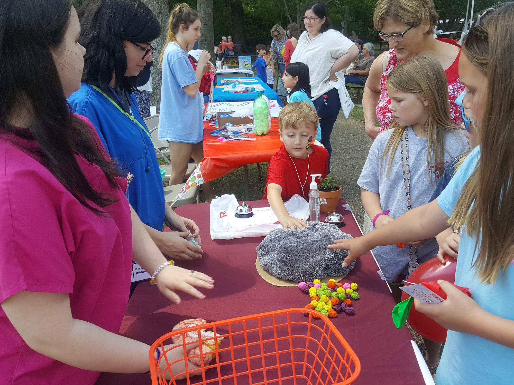 Volunteer teenagers use a prop resembling the human brain to demonstrate brain function to children.