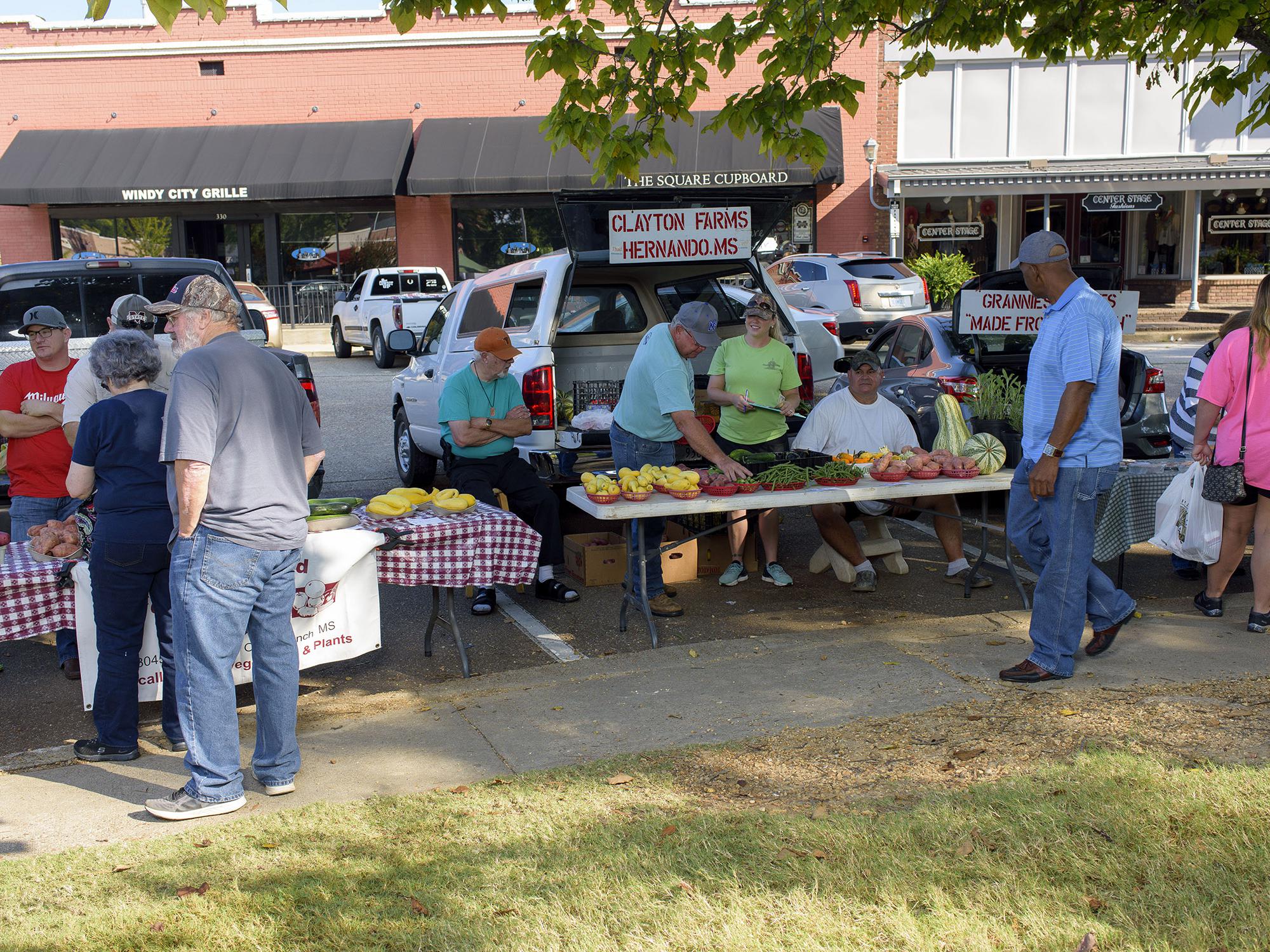 Several people gather to buy produce on display at a farmers market.