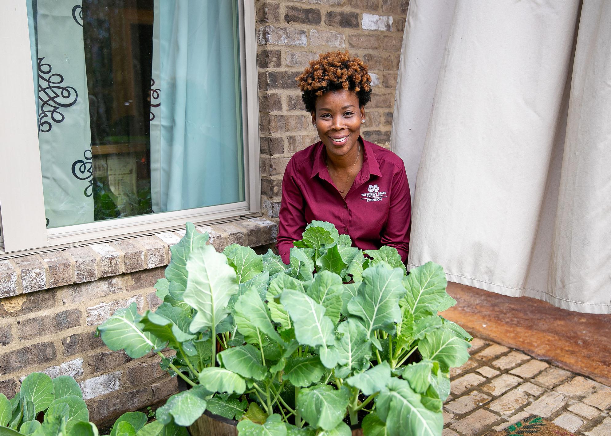 A woman kneels behind a planter on a brick patio.