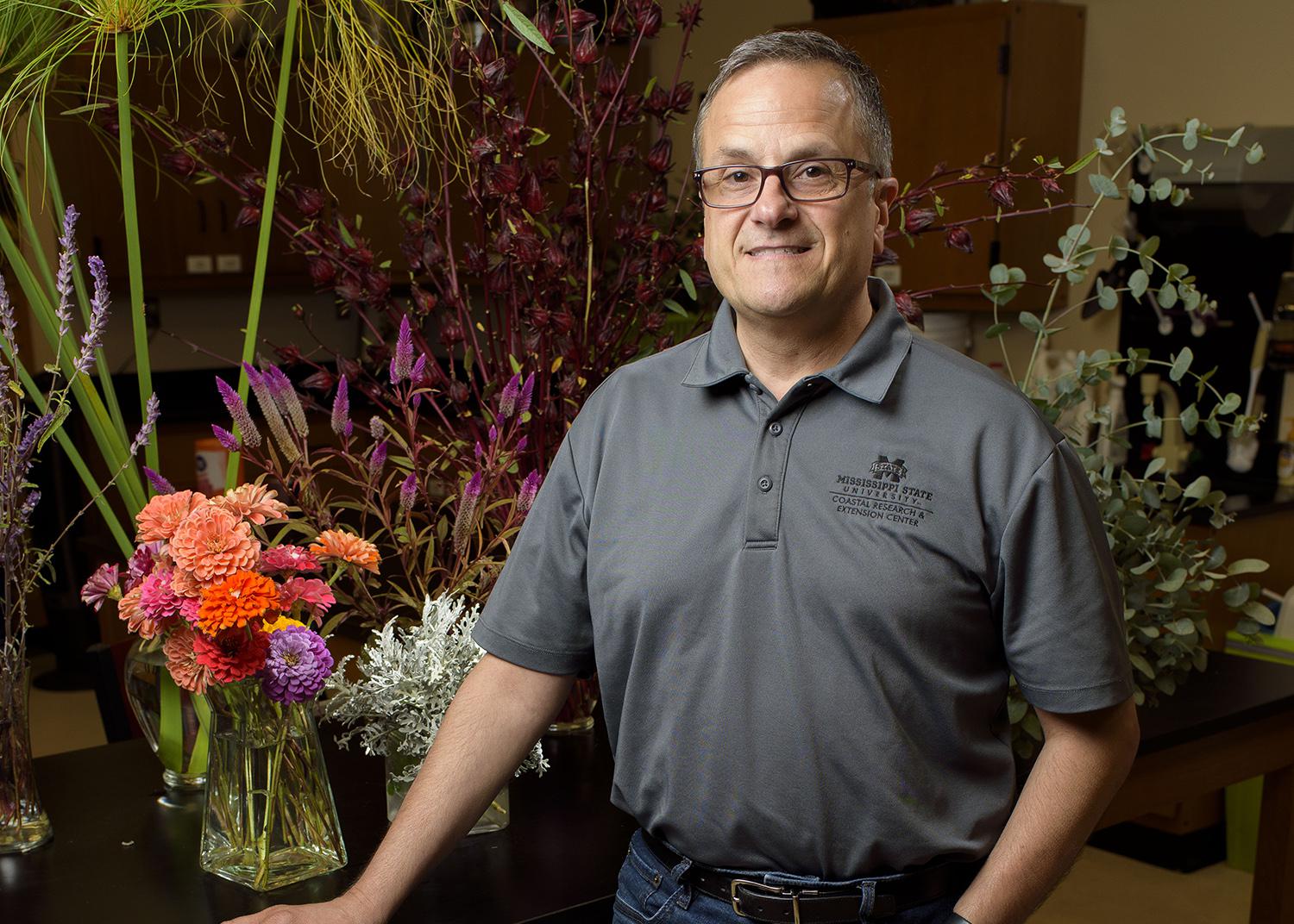 A man rests his hand on a table displaying floral arrangements.