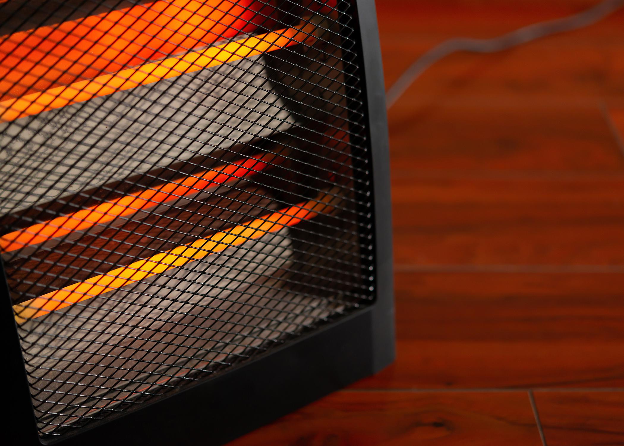 Close up of an electric space heater sitting on a hardwood floor.