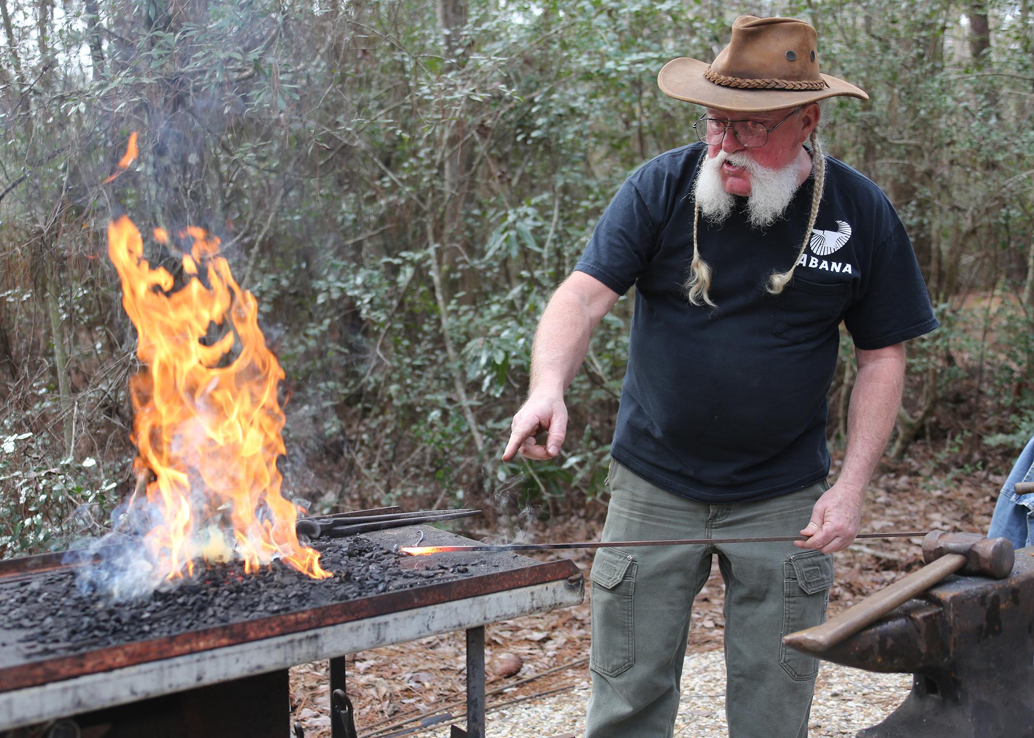 A man points at hot metal he just heated in a fire to forge it.