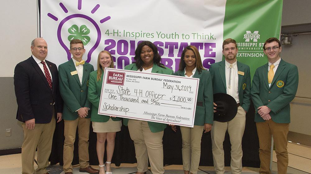 An adult with 4H'ers with a large scholarship check.