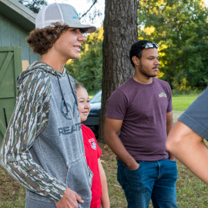 A boy wearing a baseball hat, a girl and another boy laughing outside.