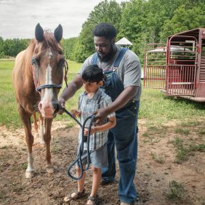 A man helps a boy with tacking for a horse.