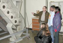 Natasha Hunter, kneeling, and fellow high school students Allen Robinson and Kristy Poole watch cotton move through a mini-gin at Mississippi State University as Eugene Columbus, a senior research associate with MSU's agriculture and biological engineering department, explains the process. The agriscience survey students visited the only operational gin on a college campus during a recent field trip.