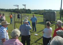 A group of adults gather outside a metal corral with electronics attached to it with a speaker inside the trap.