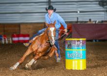 A man on a horse leans as they race around a colorful barrel.  