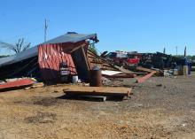 A damaged red pickup truck is visible in the middle of a collapsed metal barn.