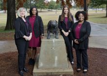 Four women stand around the Bully statue on the Mississippi State University campus.