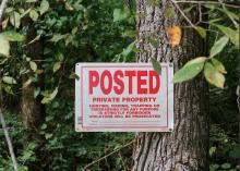 A private property sign is nailed to a tree with vegetation in the background.