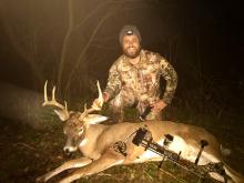 A man wearing hunting gear displays a deer he harvested with a bow and arrow.