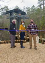 Three people stand in front of a pavilion while cutting a ceremonial ribbon.