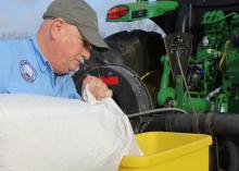 A man pours a bag into a yellow hopper on a tractor.