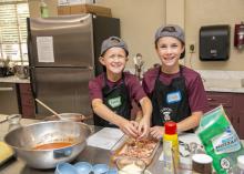 Two boys work together adding meat to a baking pan.