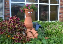 A face is painted on a human shape made of pots sitting in a garden.