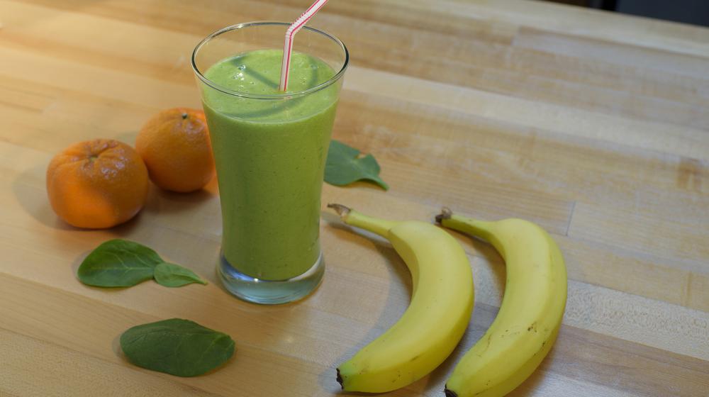 A green smoothie fills a tall clear drinking glass and has a red and white striped straw in it.  