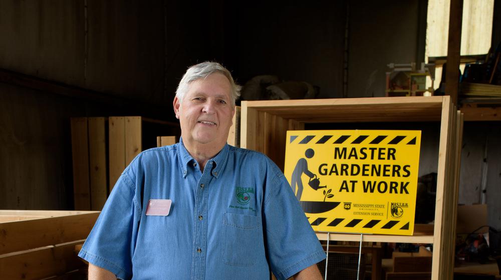 Paul Cavanaugh standing in front of a sign that reads Master Gardeners at Work.
