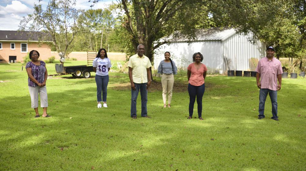 Four women and two men stand spaced out in green grass.