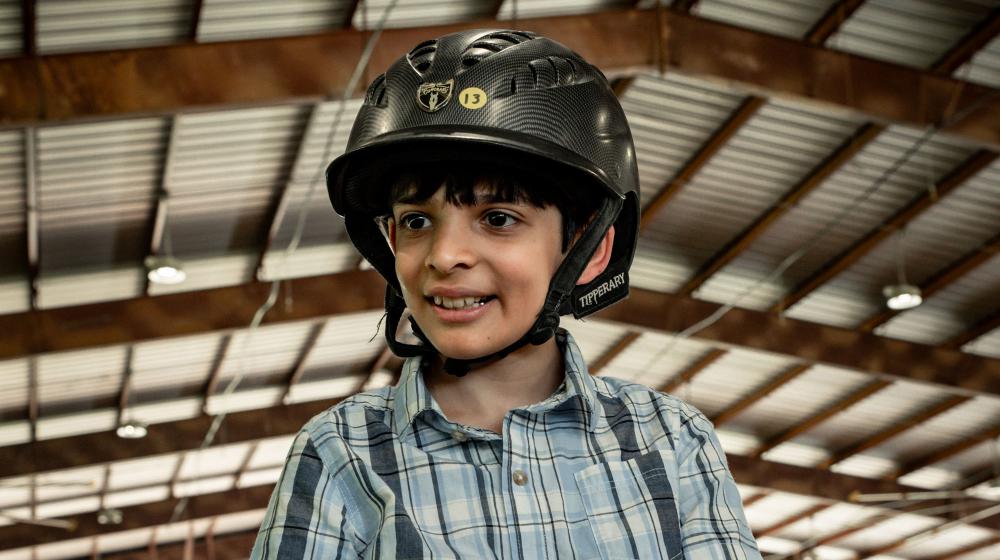 A smiling young man astride a horse and wearing a helmet.