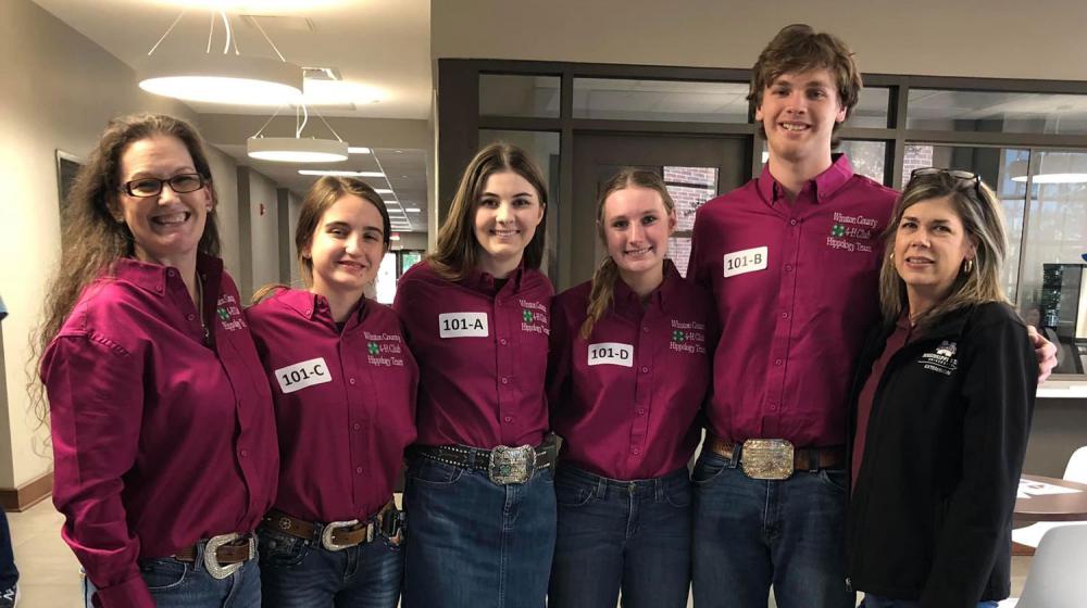 Six people, including two women, three girls, and one boy, wearing maroon polo shirts and smiling at the camera.