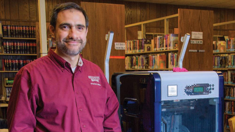 A man stands next to a 3D printer.