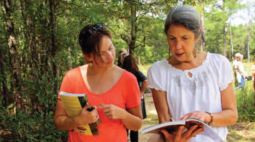 Two women walk and look at a book.