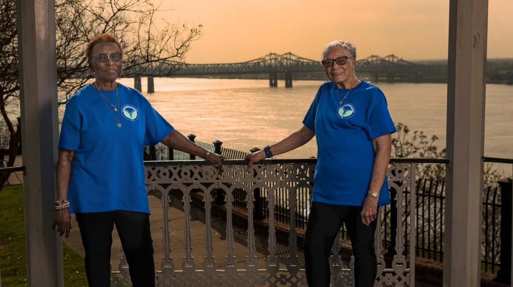 Two older women wearing blue MHV t-shirts sitting at a table overspread with papers.