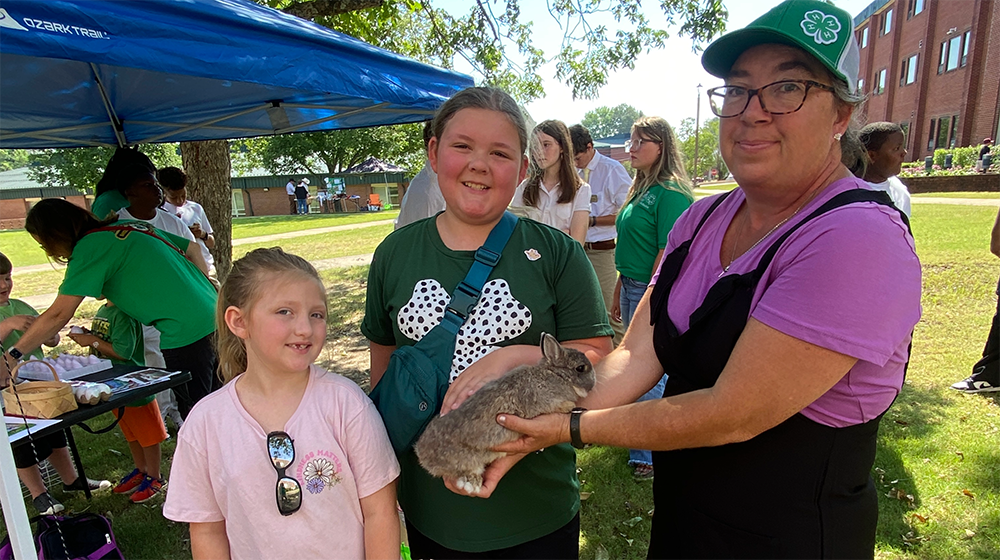 A woman showing a rabbit to two girls at a 4-H event.