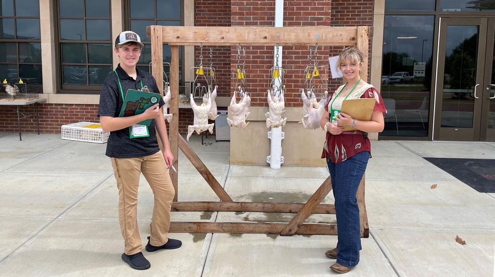 Two youth standing in front of butchered chickens.