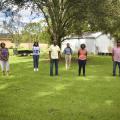 Four women and two men stand spaced out in green grass.