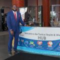 A man wearing a suit stands beside a desk with a banner listing “Welcome to the Tunica Health & Wellness Hub.”