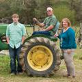 An older man, a woman, and a teenage boy around a green tractor.