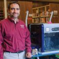 A man stands next to a 3D printer.