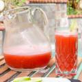 A clear glass pitcher and glass with watermelon punch. 