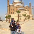 A Black man and woman standing with a boy and a girl in front of a mosque in the desert.